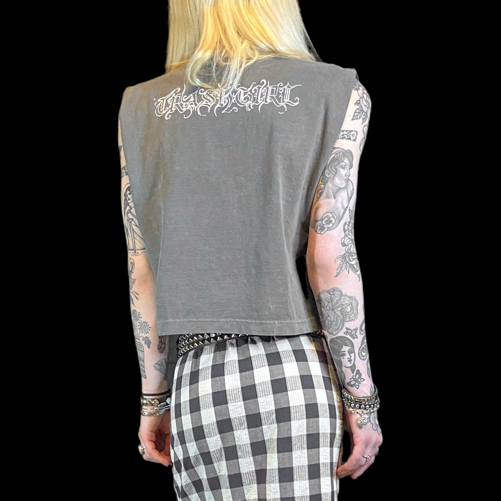 Person wearing a sleeveless gray top with text on the back, checkered pants, and tattoos.