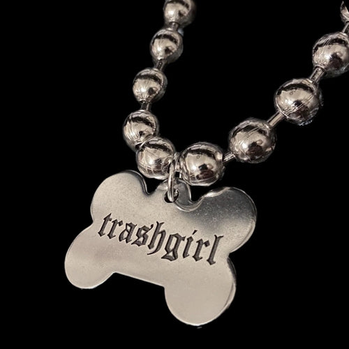 Silver necklace with a bone-shaped pendant displaying 'trashgirl' on a black background