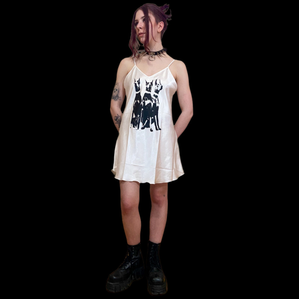 Person wearing white sleeveless slip dress with a black design of 3 doberman dogs. 