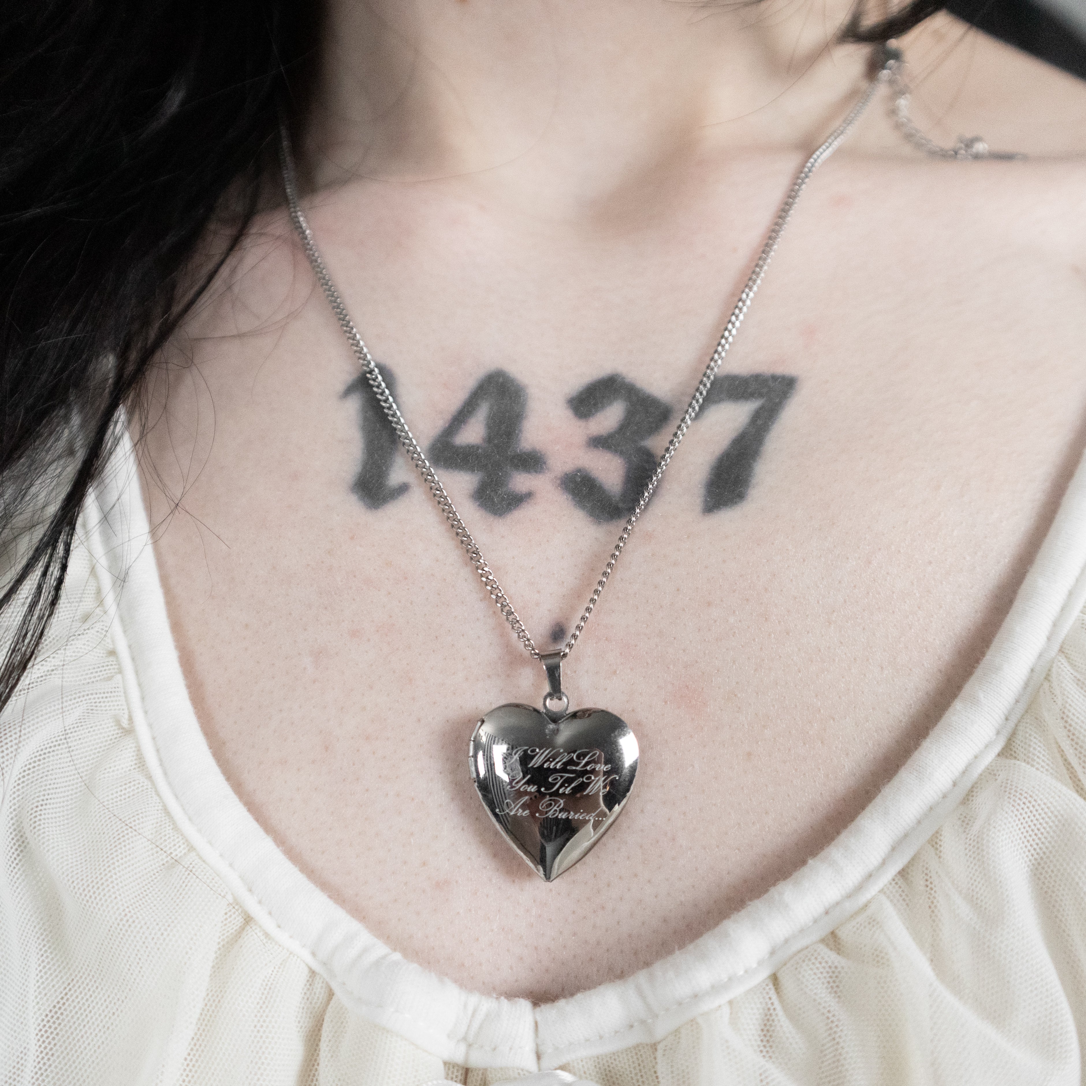 Heart-shaped silver pendant necklace worn by a person with a tattoo on their neck.
