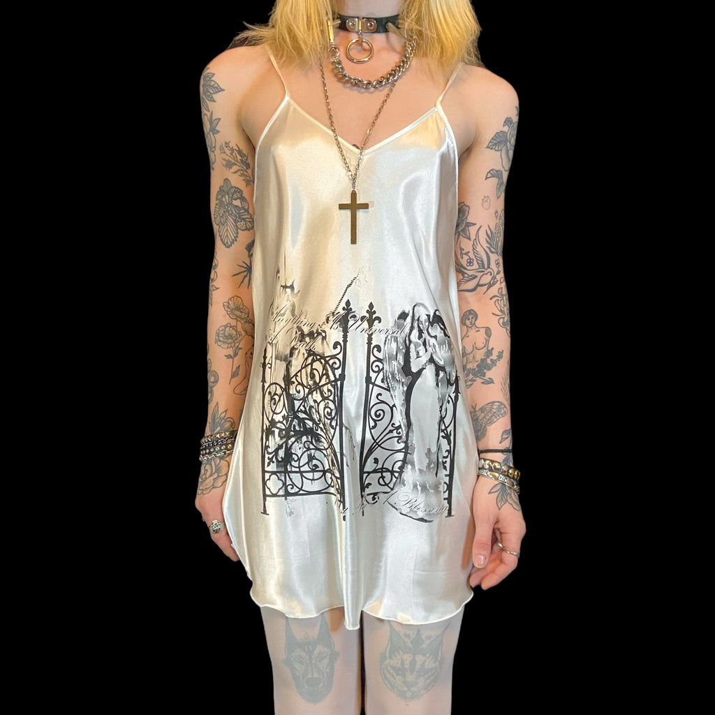 Person wearing a white slip dress with black designs on a plain background