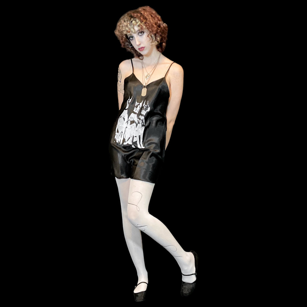 Model wearing a black satin outfit with white stockings on a plain background.
