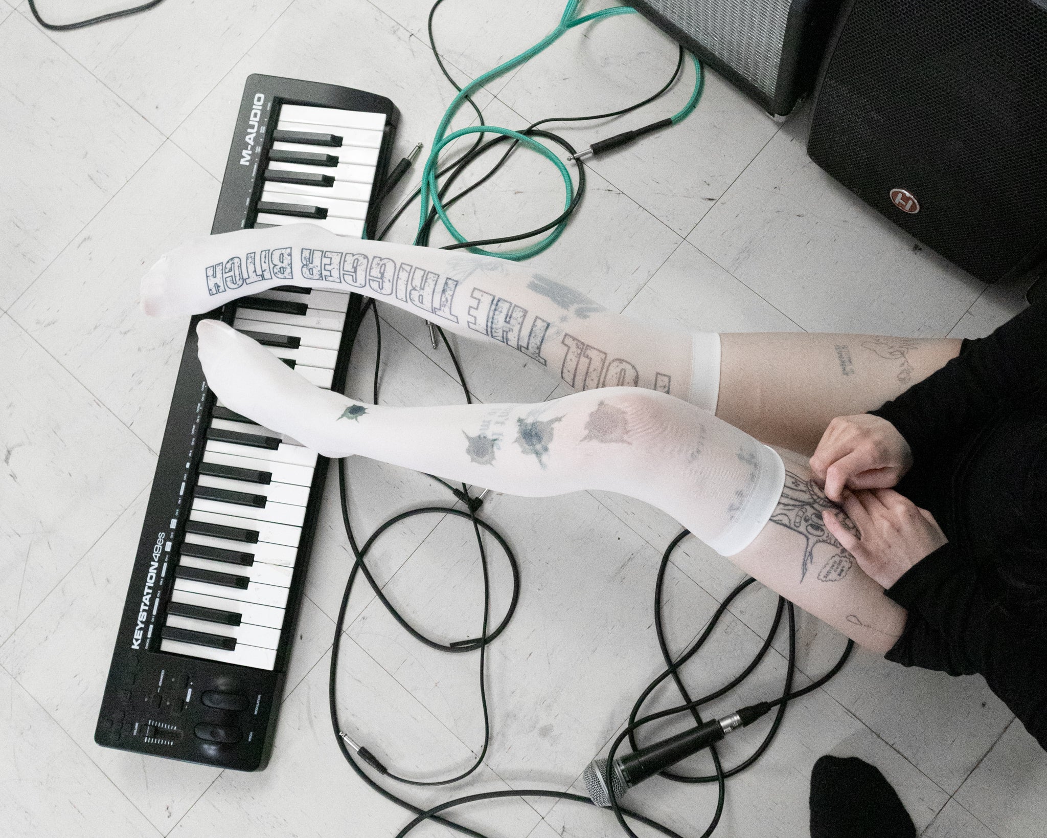 Person with tattoos sitting on a floor with a keyboard and amplifier