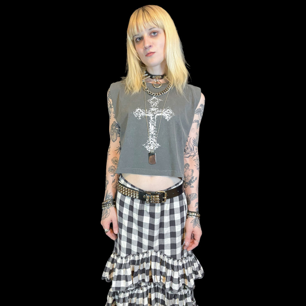 Person wearing a sleeveless top with a cross design and a checkered skirt on a black background