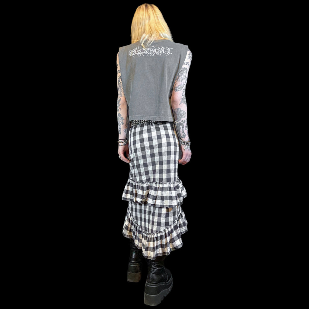 Person wearing a sleeveless gray top with text and a black and white checkered skirt on a plain background