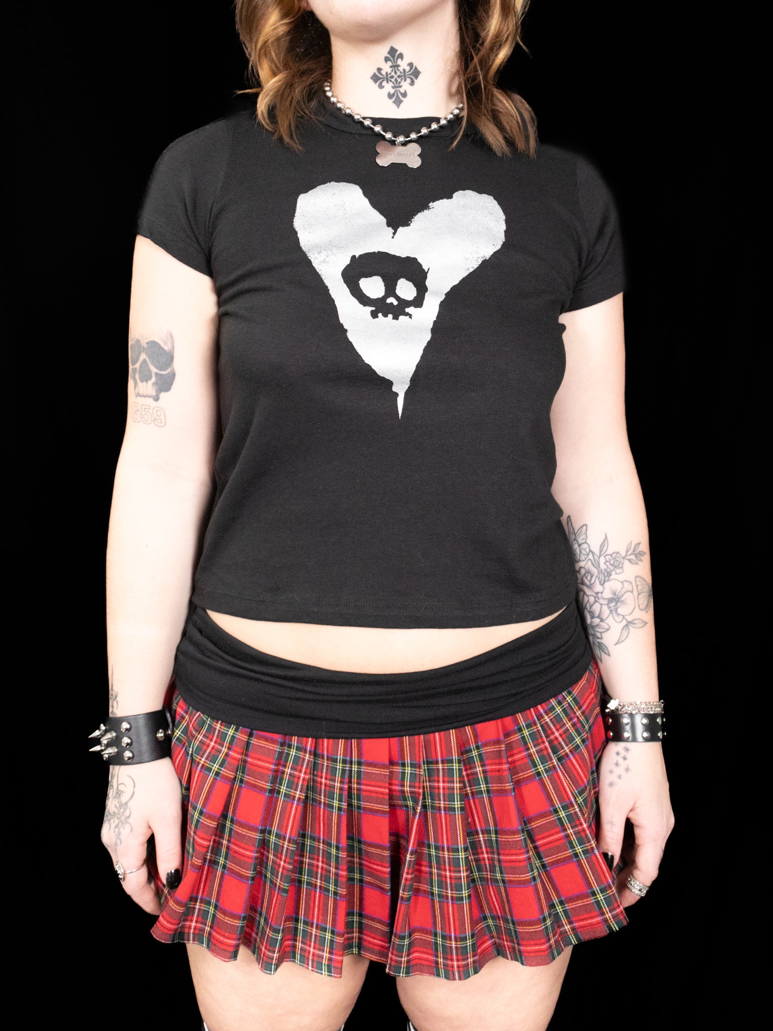 Person wearing a black t-shirt with a skull and crossbones design and a red plaid skirt on a black background