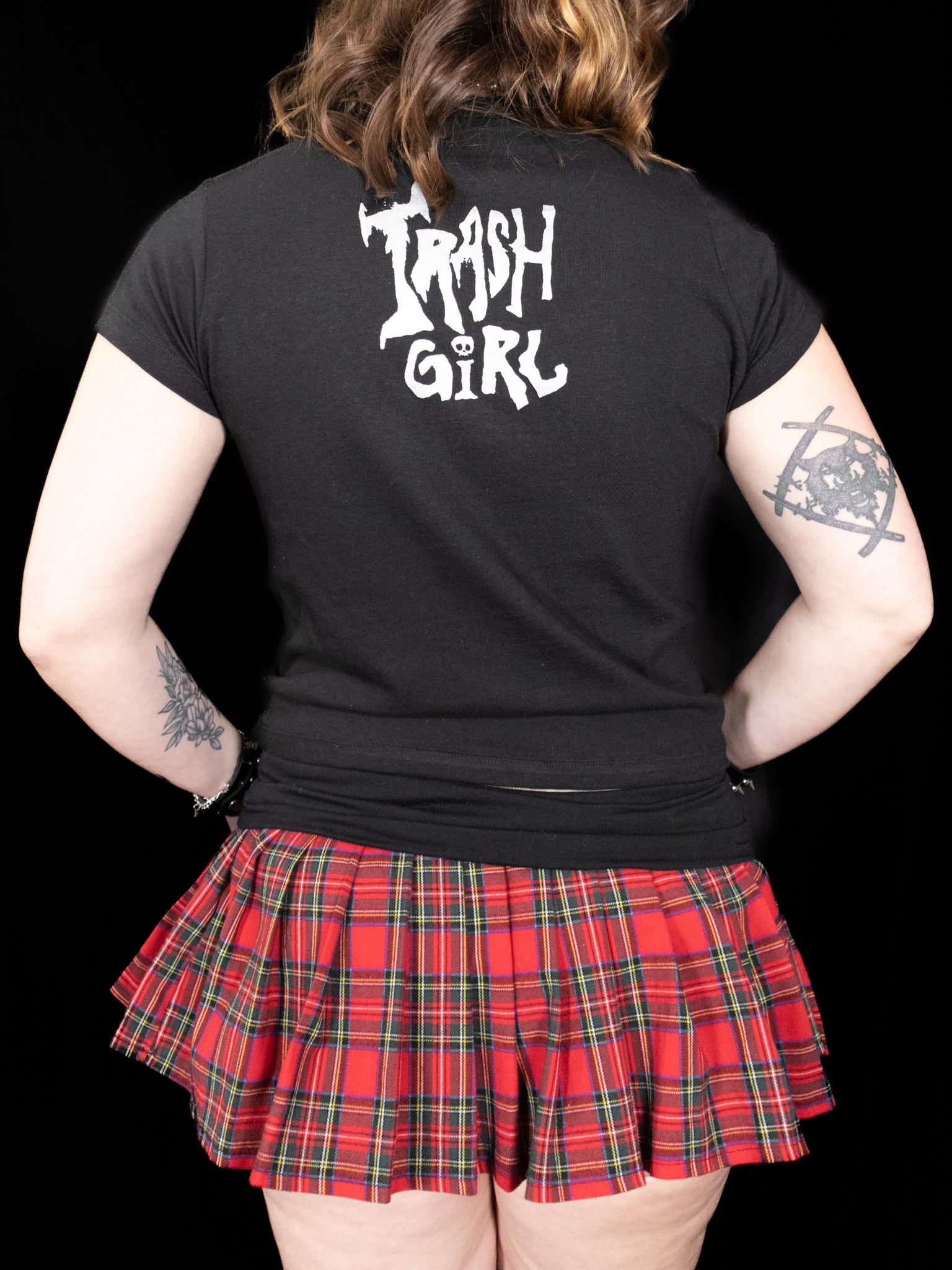 Person wearing a black t-shirt with 'Trash Girl' text and a red plaid skirt on a black background