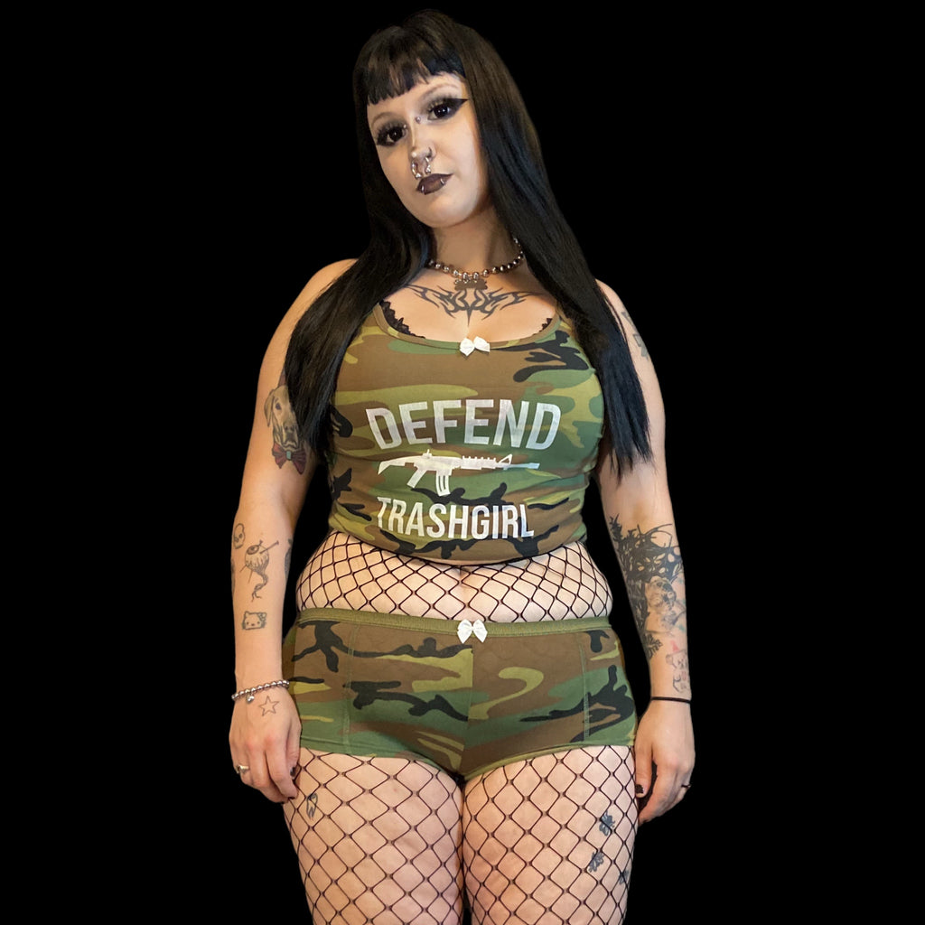 Person wearing a camouflage outfit with 'Defend Trashgirl' text on a black background