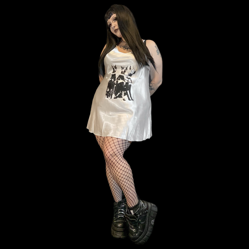 Person wearing a white dress with black designs and fishnet stockings on a plain background