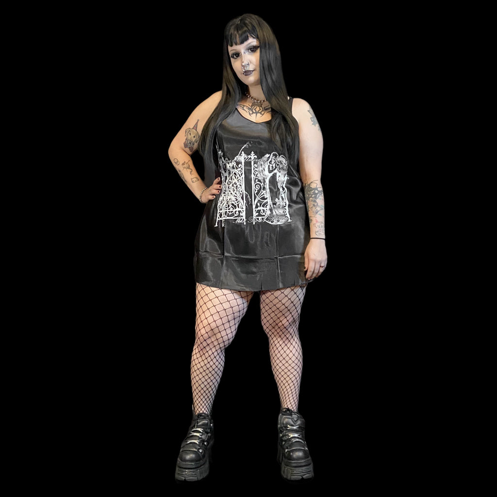 Person wearing a black tslip dress with white graphic design, fishnet stockings, and black shoes on a black background.