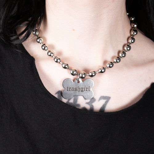 Necklace with a bone-shaped pendant labeled 'trashgirl' on a black background