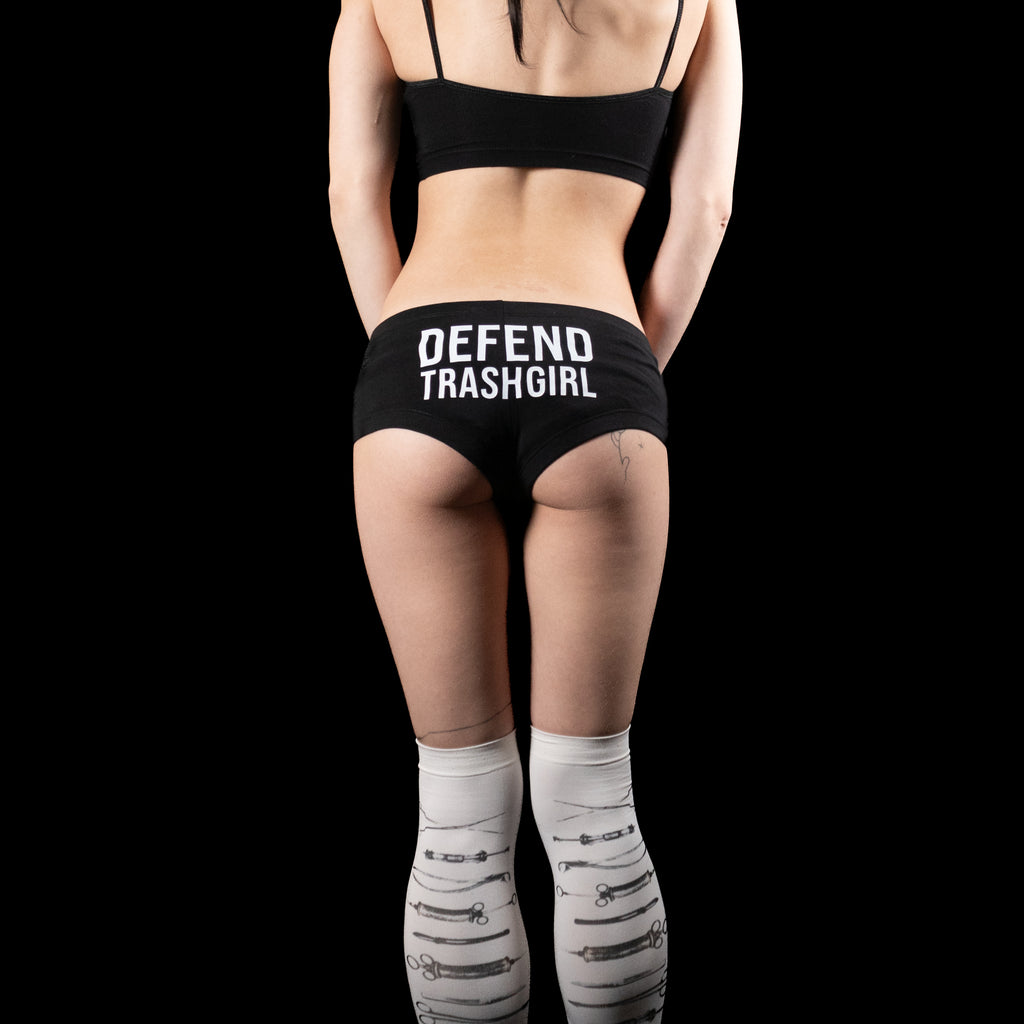 Person wearing black underwear with 'DEFEND TRASHGIRL' text on a plain background