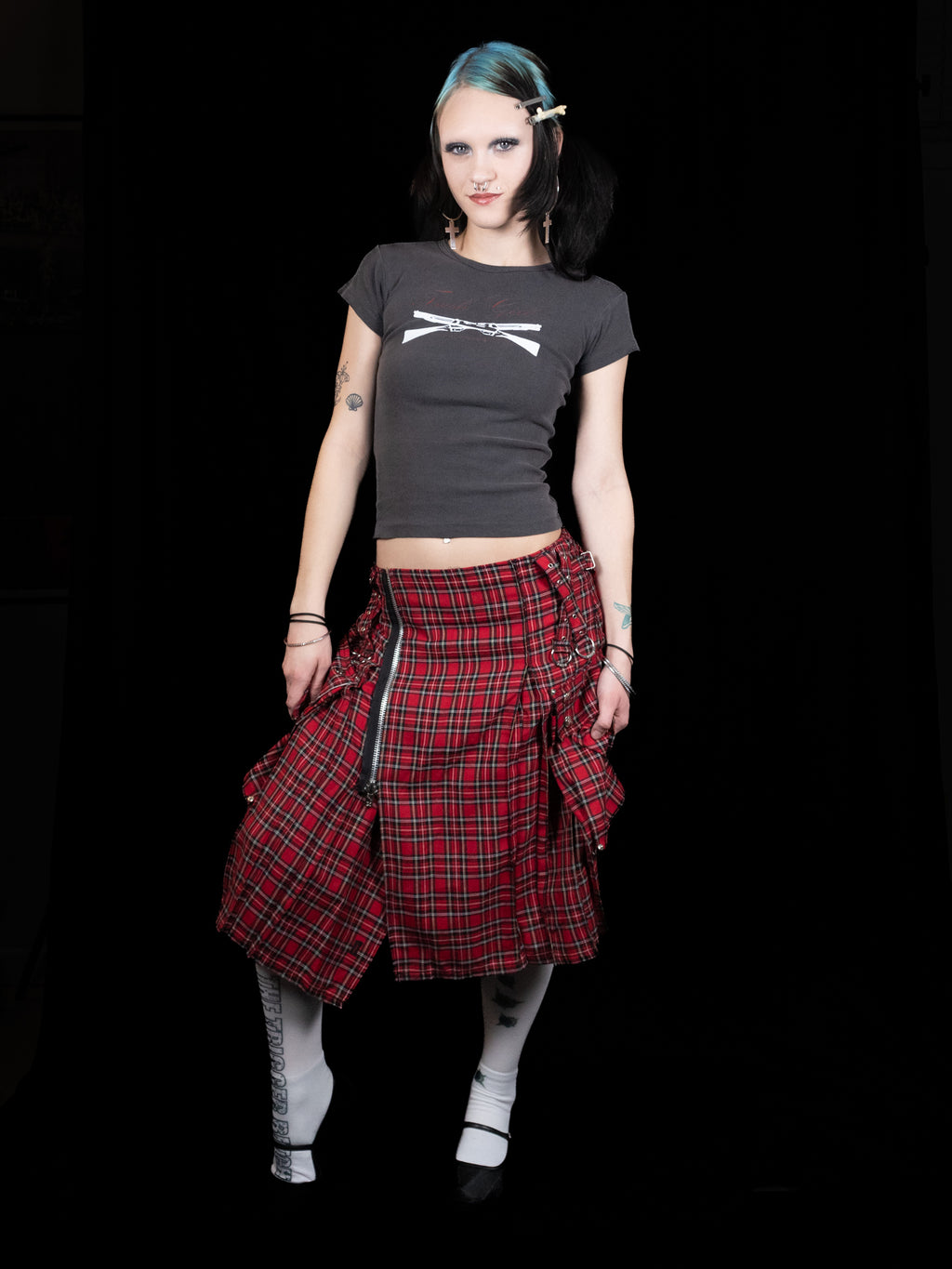 Person wearing a black t-shirt and red plaid skirt on a black background
