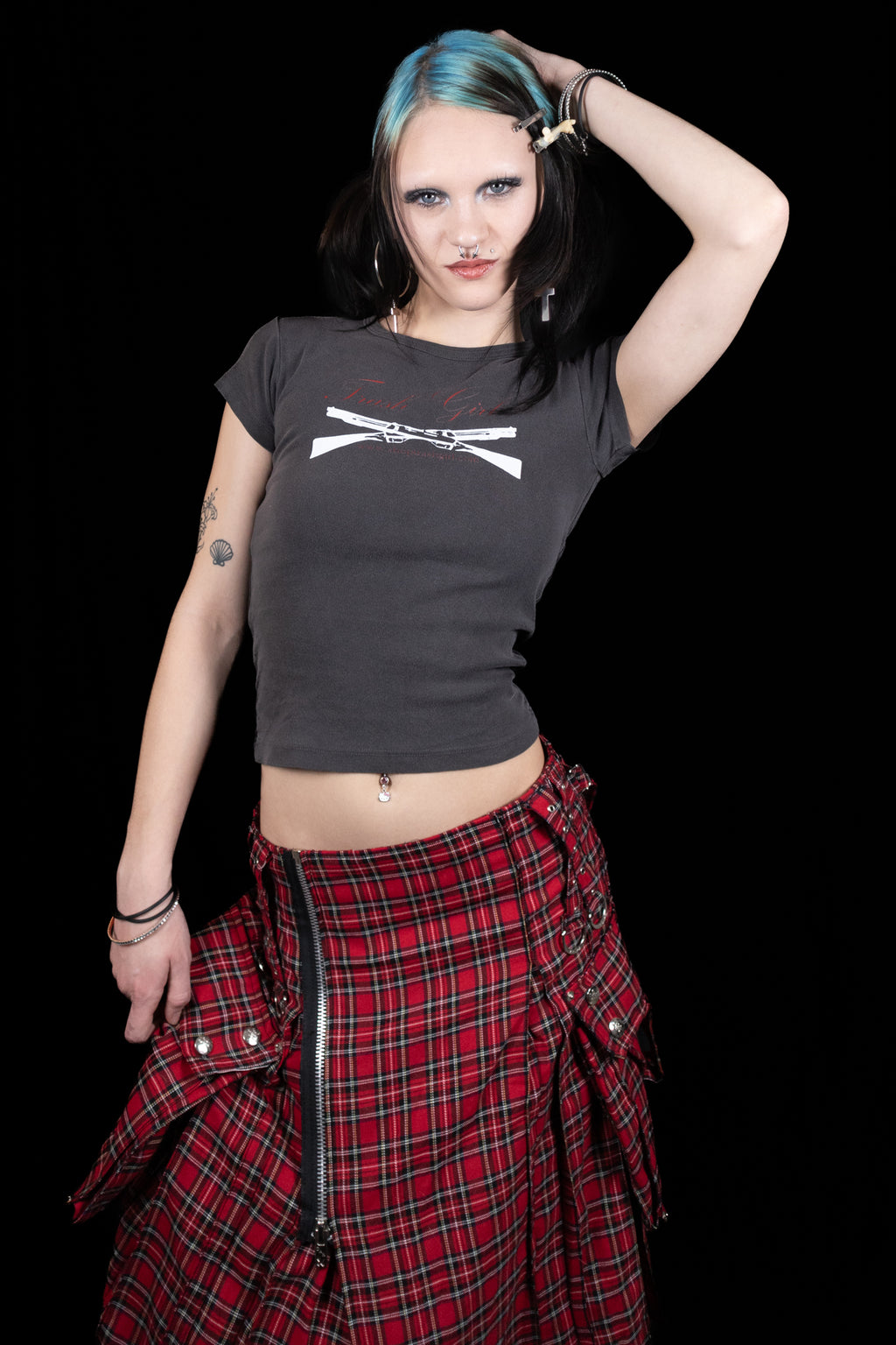 Person wearing a black crop top with a graphic design and a red plaid skirt on a black background