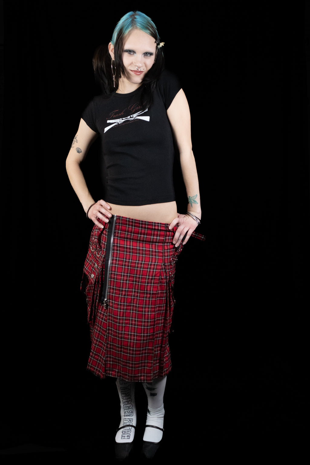 Person wearing a black t-shirt with a graphic design and a red plaid skirt on a black background