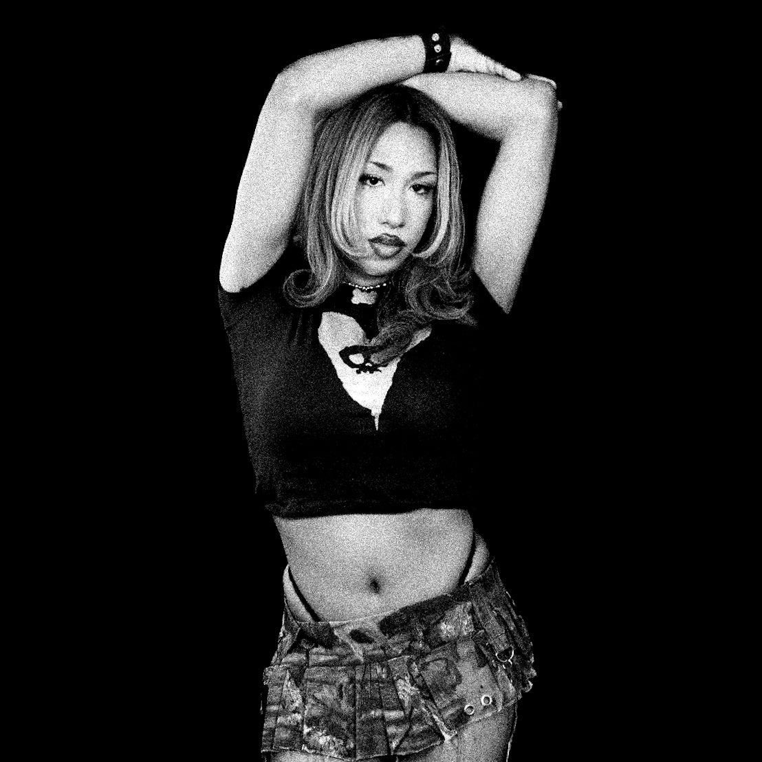 Black and white photo of a person posing with arms above head against a black background