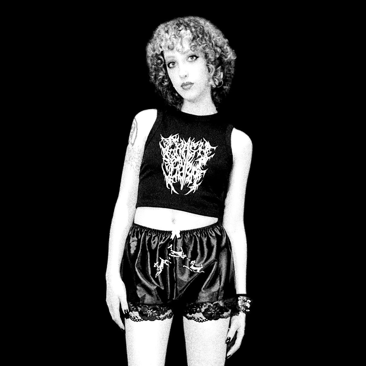 Black and white photo of a person wearing a sleeveless top with a graphic design and patterned shorts.
